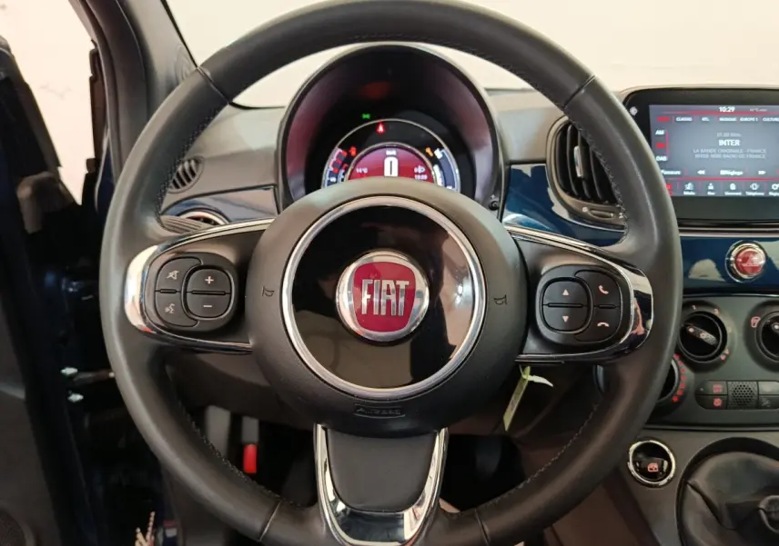Vue rapprochée du volant en cuir noir avec logo FIAT, tableau de bord et écran tactile bleu de la Fiat 500 Hybrid 2022.