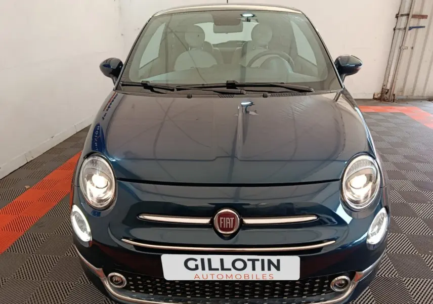 Vue avant d'une Fiat 500 Dolcevita hybride bleu foncé avec phares allumés dans un garage.