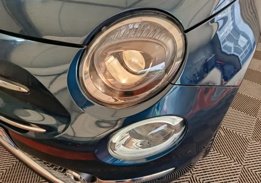 Gros plan sur le phare avant droit bleu métallisé de la Fiat 500 Hybrid Dolcevita 2022 avec détails chromés.