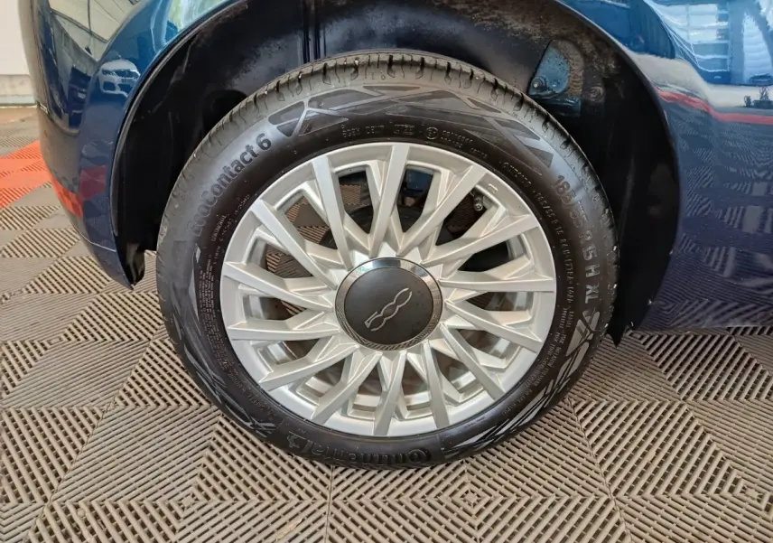Gros plan sur la roue arrière droite d'une FIAT 500 Dolcevita bleu, avec passage de roue et partie de la carrosserie visibles.