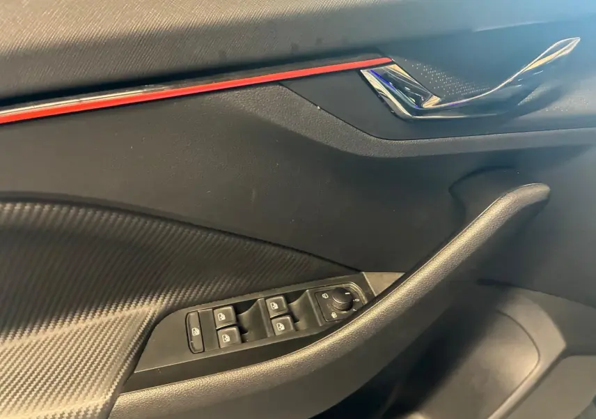 Détail de la porte avant gauche du Skoda Kamiq 2024 gris foncé, avec commandes des vitres et bande décorative rouge.