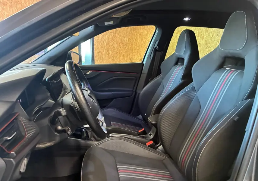 Vue intérieure côté conducteur du Skoda Kamiq 2024 gris foncé, mettant en valeur les sièges sport noirs avec bandes rouges et blanches.