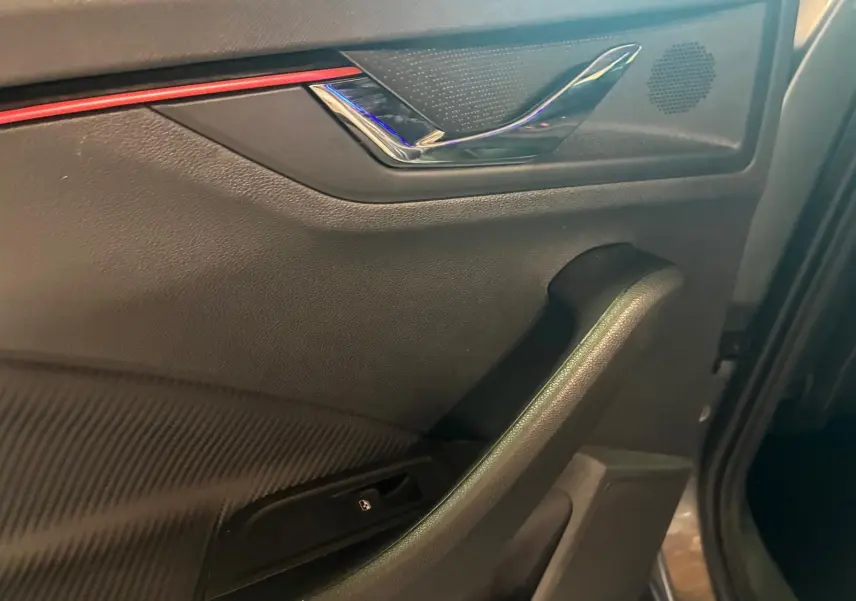 Détail de la porte côté gauche intérieure du Skoda Kamiq 2024 finition Monte-Carlo avec insert rouge et poignée chromée.