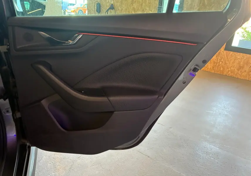 Intérieur de la porte arrière gauche du Skoda Kamiq 2024 gris foncé, avec bande lumineuse rouge et finition texturée.