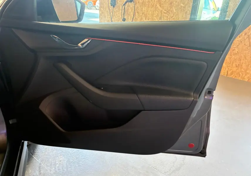 Vue intérieure de la porte avant gauche du Skoda Kamiq gris foncé 2024, avec bande décorative rouge et poignée chromée.