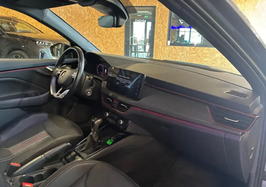 Vue intérieure côté conducteur du Skoda Kamiq 2024 gris foncé, avec tableau de bord noir et éclairage d'ambiance rouge.