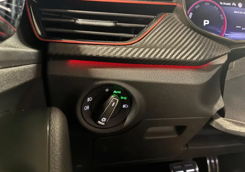 Gros plan sur le bouton de commande des phares avec éclairage vert, tableau de bord noir et insert effet carbone du Skoda Kamiq 2024.
