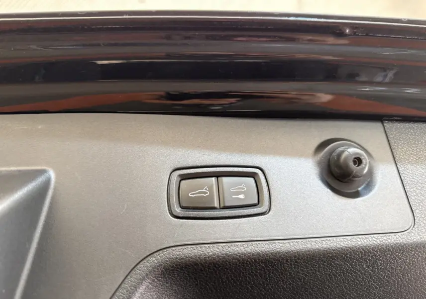 Gros plan sur les boutons d'ouverture électrique du coffre et du hayon sur la porte arrière noire d'une Porsche Panamera 4 E-Hybrid Sport Turismo.