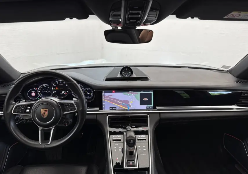 Vue intérieure avant du tableau de bord noir de la Porsche Panamera 4 E-Hybrid Sport Turismo avec écran tactile de navigation.