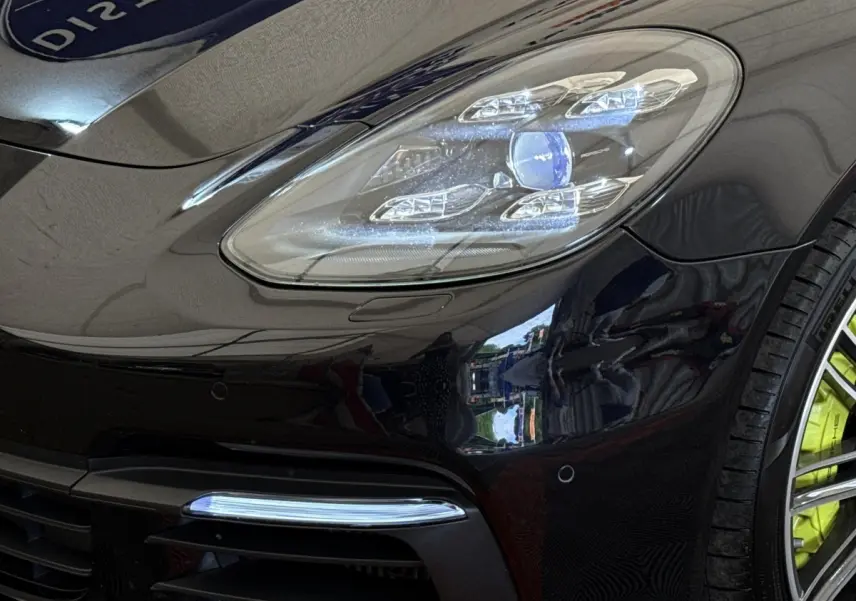 Gros plan sur l'avant droit noir brillant d'une Porsche Panamera 4 E-Hybrid Sport Turismo, avec phares LED et jante verte.