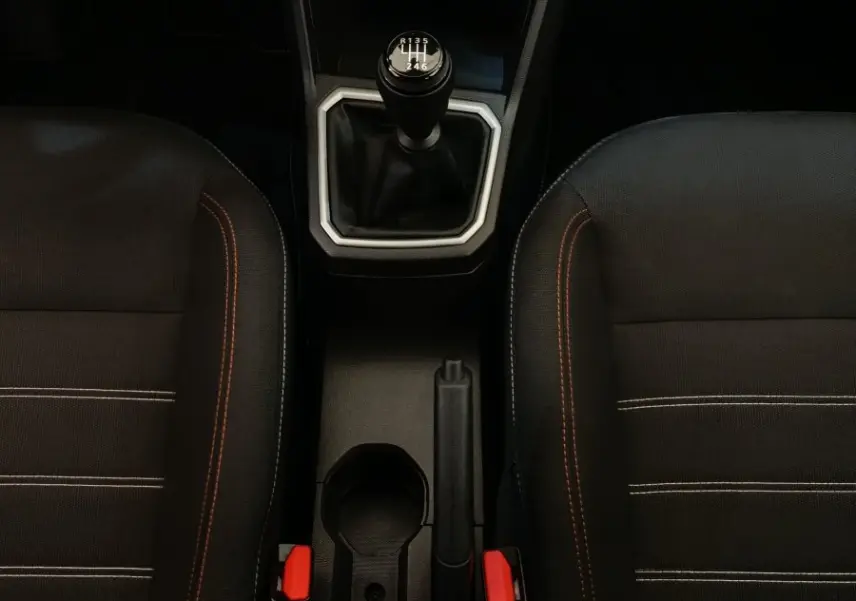Vue plongeante sur la console centrale intérieure de la Dacia Sandero gris clair, avec levier de vitesse manuel et sièges noirs à surpiqûres orange.