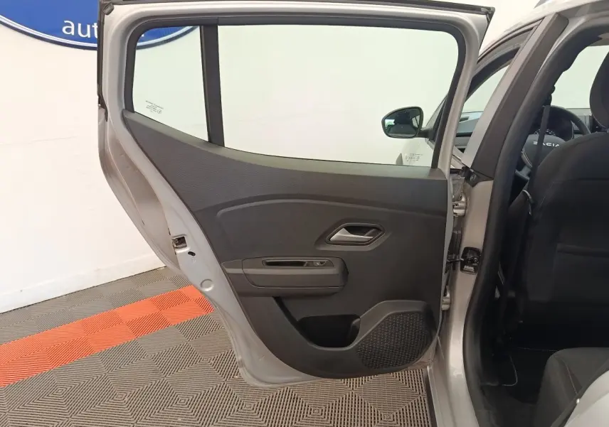 Vue côté gauche sur la porte arrière ouverte d'une Dacia Sandero gris clair, montrant l'intérieur noir et la poignée de porte.