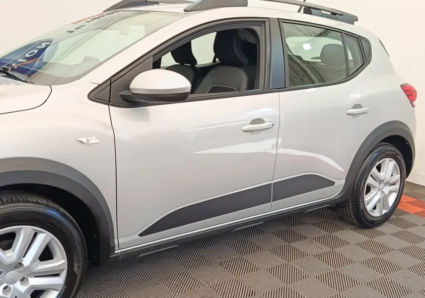 Vue latérale droite d'une Dacia Sandero Expression gris clair avec protections noires et jantes argentées.