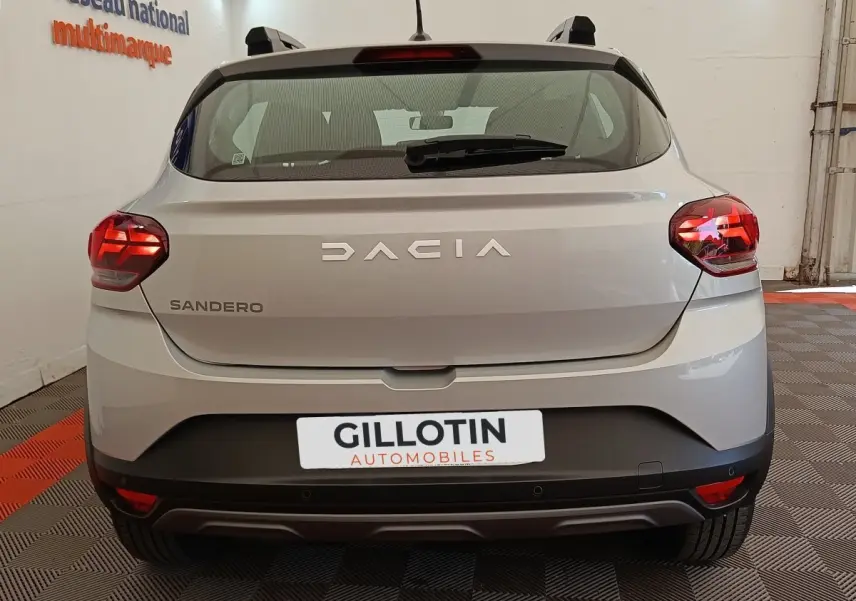 Vue arrière d'une Dacia Sandero gris clair 2023 avec feux LED et logo DACIA bien visible.
