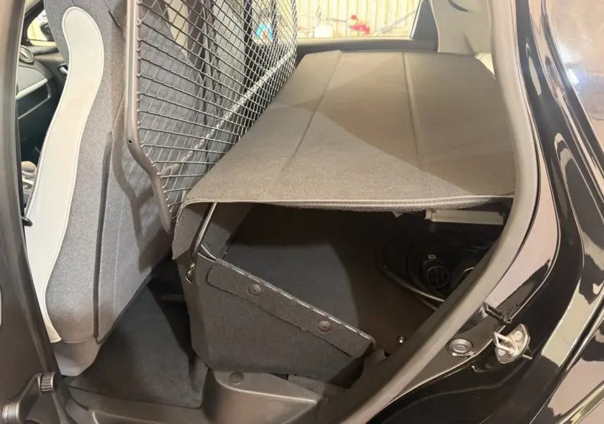 Vue intérieure côté droit du coffre ouvert de la Renault ZOE noire 2024 avec filet de séparation et câble de charge visible.