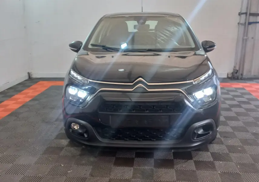 Vue frontale d'une Citroën C3 noire 2024 avec phares LED allumés et calandre distinctive en intérieur.