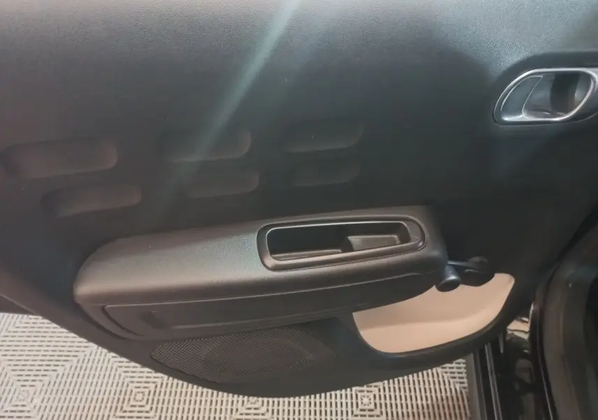 Vue rapprochée de la porte intérieure côté droit de la Citroën C3 noire, avec poignée et manivelle de vitre manuelle.