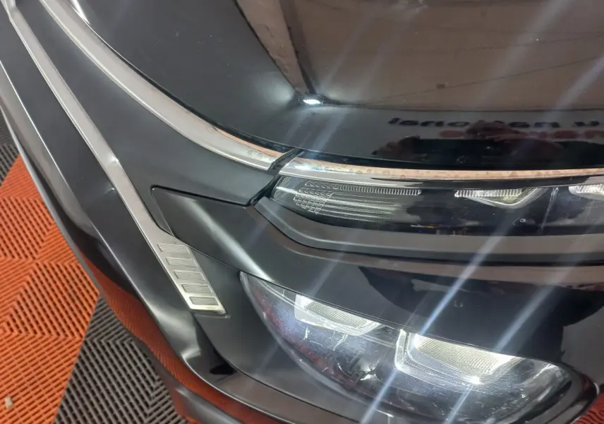 Gros plan sur le phare avant droit noir brillant de la Citroën C3 2024 avec détails chromés et éclairage LED allumé.