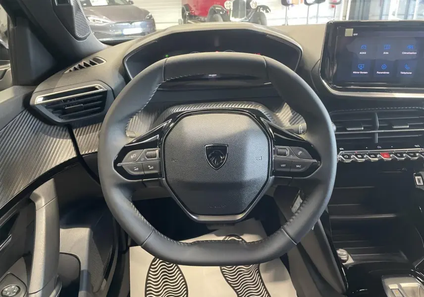 Vue centrée sur le volant compact Peugeot 2008 avec tableau de bord et écran tactile, intérieur noir et décor carbone.