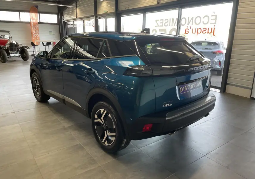 Peugeot 2008 bleu 3/4 arrière droit en intérieur, jantes alliage bicolores et feux arrière LED 3 griffes visibles.