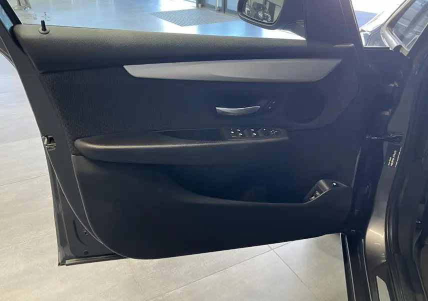 Gros plan sur la porte côté gauche d'une BMW Série 2 225xe Active Tourer grise, montrant les commandes de vitres et la poignée intérieure.