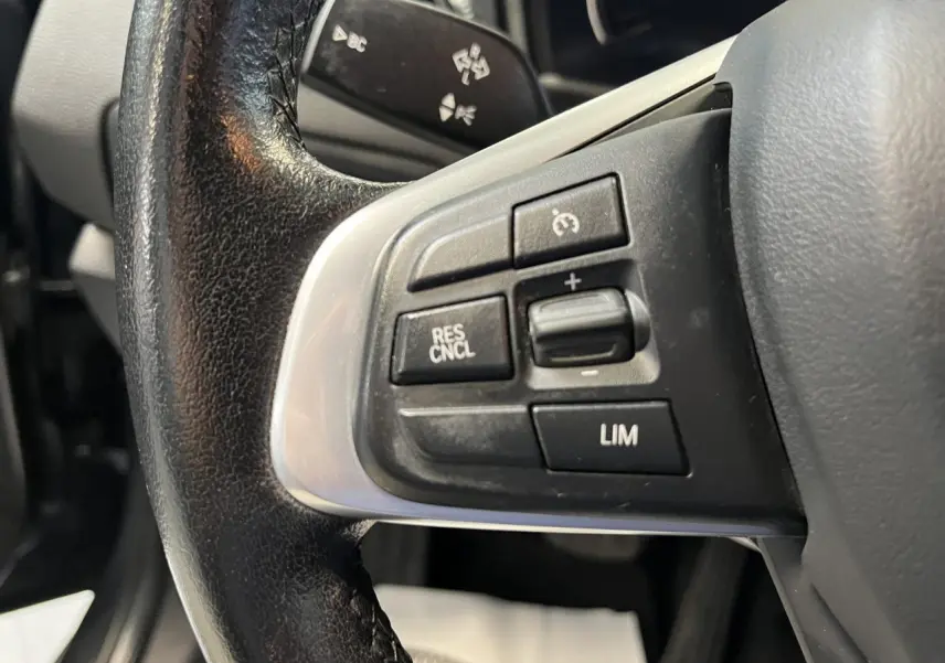 Gros plan sur les commandes de régulateur de vitesse au volant cuir noir d'une BMW Série 2 Active Tourer gris 2018.