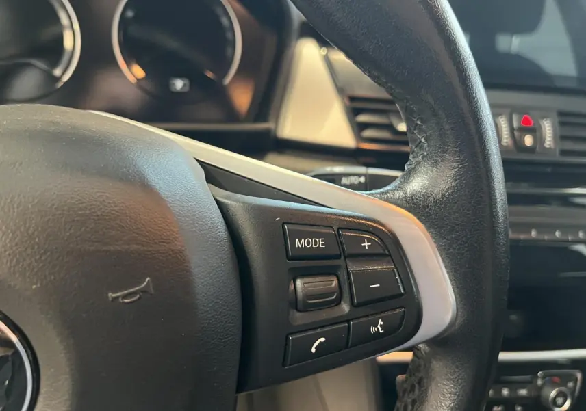 Gros plan sur les commandes du volant cuir noir d'une BMW Série 2 225xe Active Tourer gris, modèle 2018.