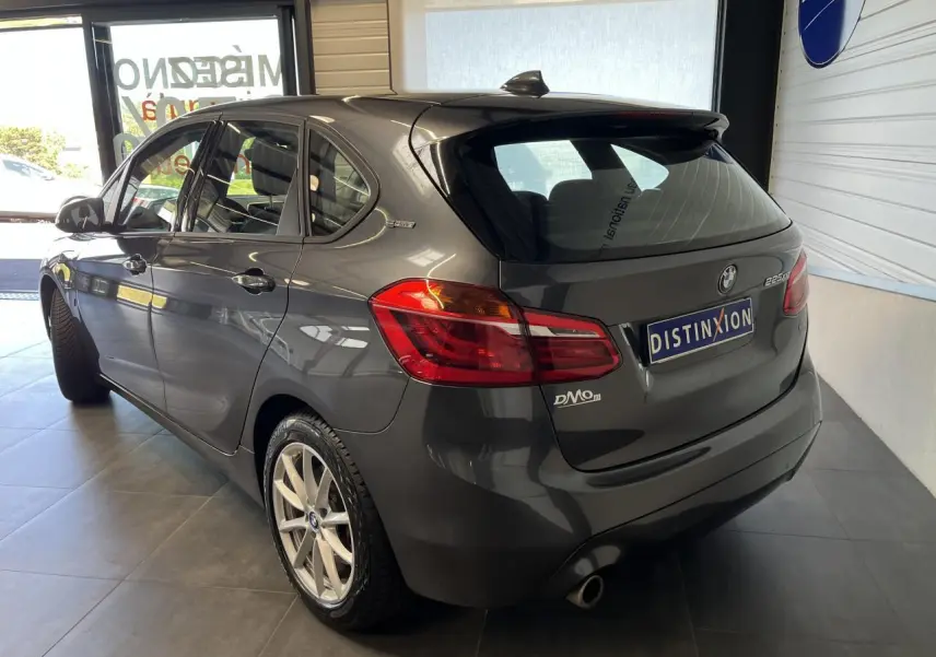 BMW Série 2 225xe Active Tourer gris vue 3/4 arrière droit en intérieur avec jantes argentées et badge hybride.