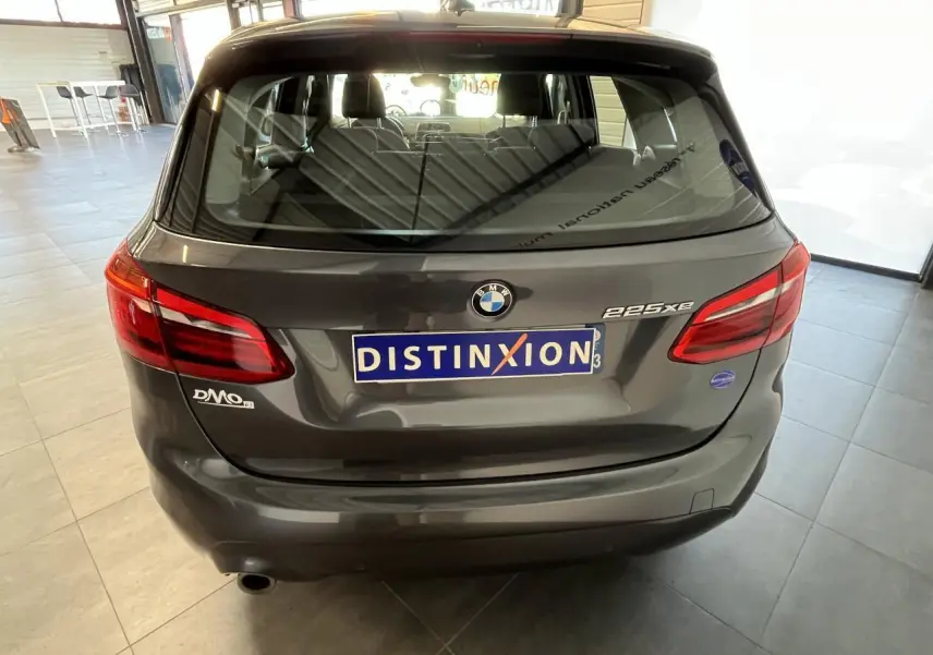 Vue arrière d'une BMW Série 2 225xe Active Tourer grise, avec logo et plaques distinctives visibles en intérieur showroom.