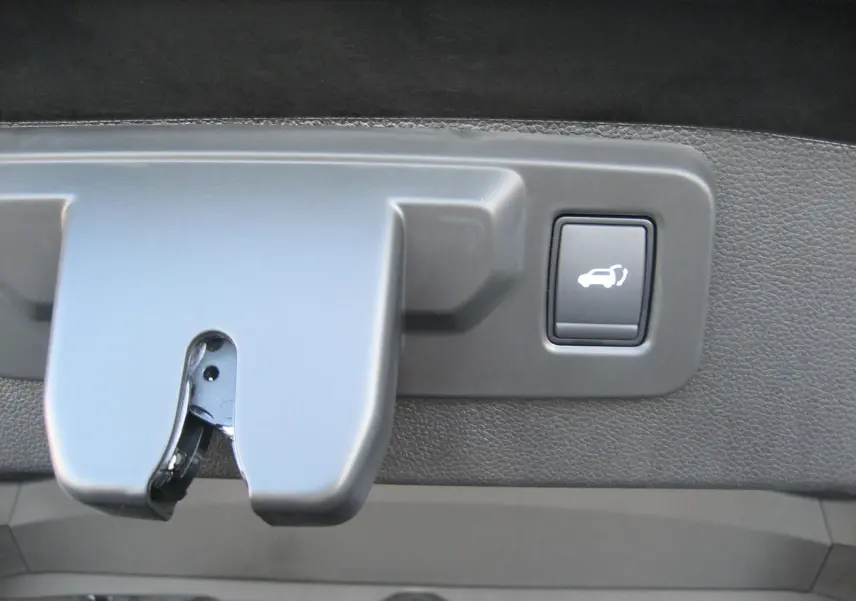 Gros plan sur le bouton d'ouverture électrique du coffre du Renault Austral gris schiste, intérieur du hayon visible.