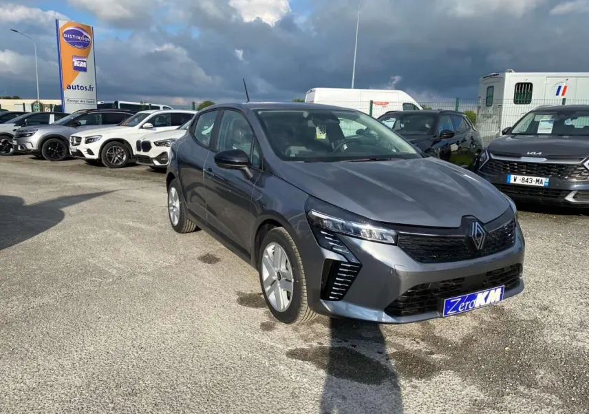 Renault Clio gris schiste vue 3/4 avant droit sur parking, mettant en valeur ses phares LED et sa calandre noire.