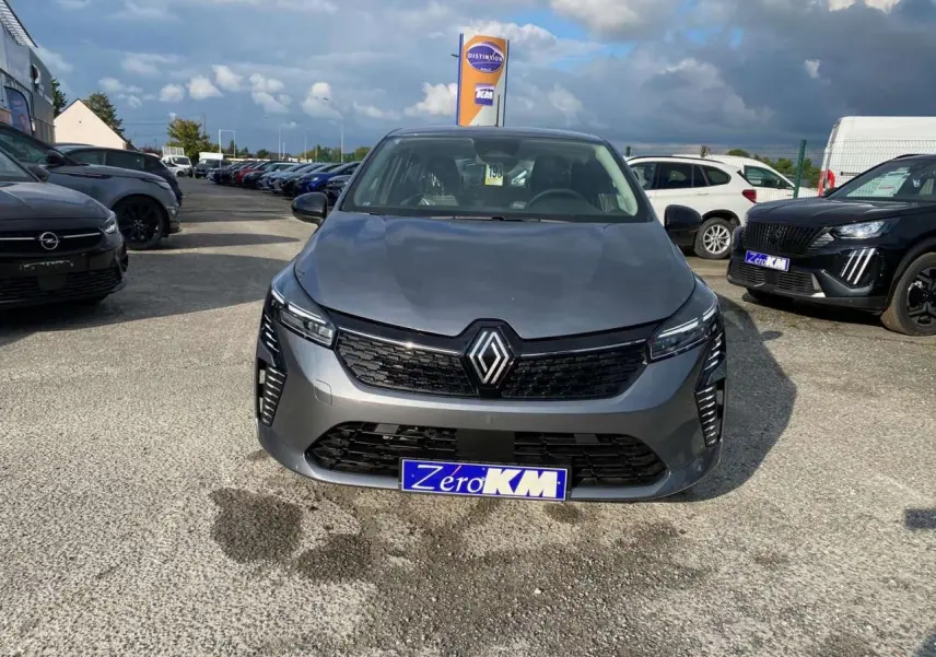 Renault Clio gris schiste vue de face sur parking, avec calandre noire et phares LED distinctifs allumés.