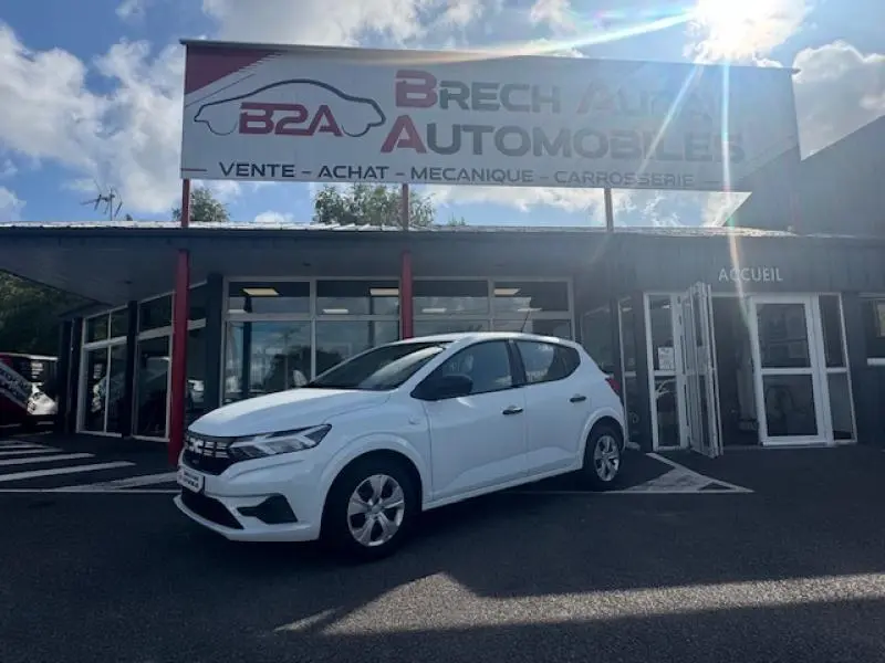 Vue 3/4 avant gauche d'une Dacia Sandero blanche 2024 garée devant un garage Brech Automobiles.