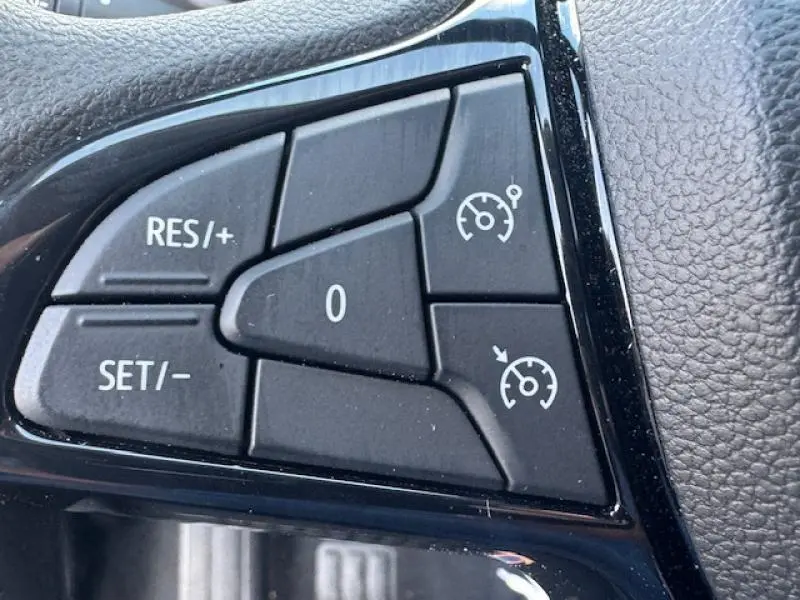 Gros plan sur les commandes du régulateur de vitesse au volant d'une Dacia Sandero blanche Essential 2024.