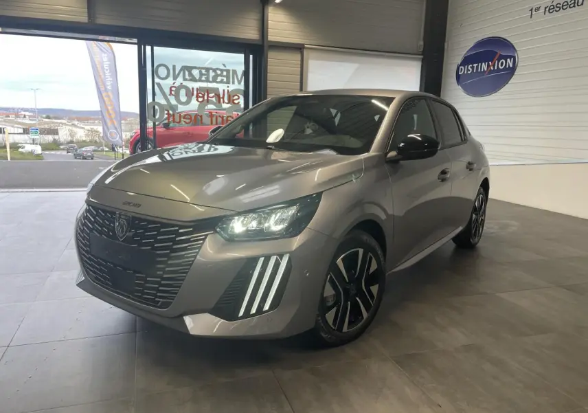 Peugeot 208 gris Artense vue 3/4 avant droit, avec calandre noire et feux LED allumés en showroom.