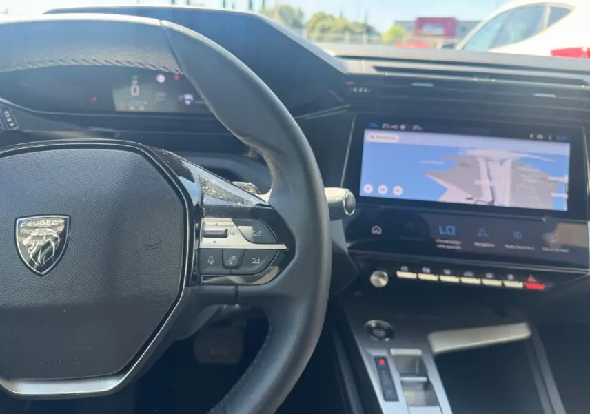 Vue intérieure du tableau de bord et volant de la Peugeot 308 Hybrid gris, avec écran tactile et commandes au volant visibles.