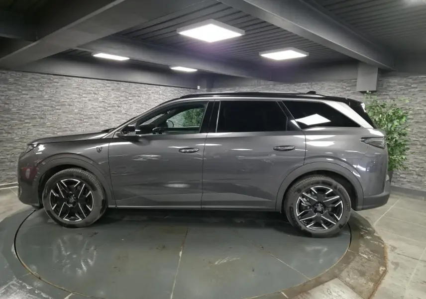 Vue de profil côté gauche du SUV Peugeot 5008 gris métallisé, avec jantes alliage noires et toit noir.