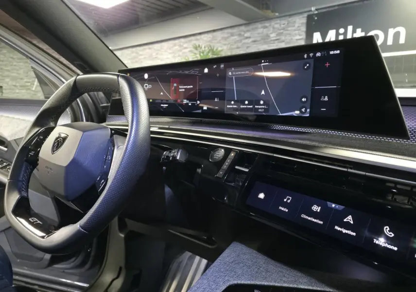 Vue intérieure côté conducteur du Peugeot 5008 gris 2025, avec volant compact GT et écran panoramique incurvé.