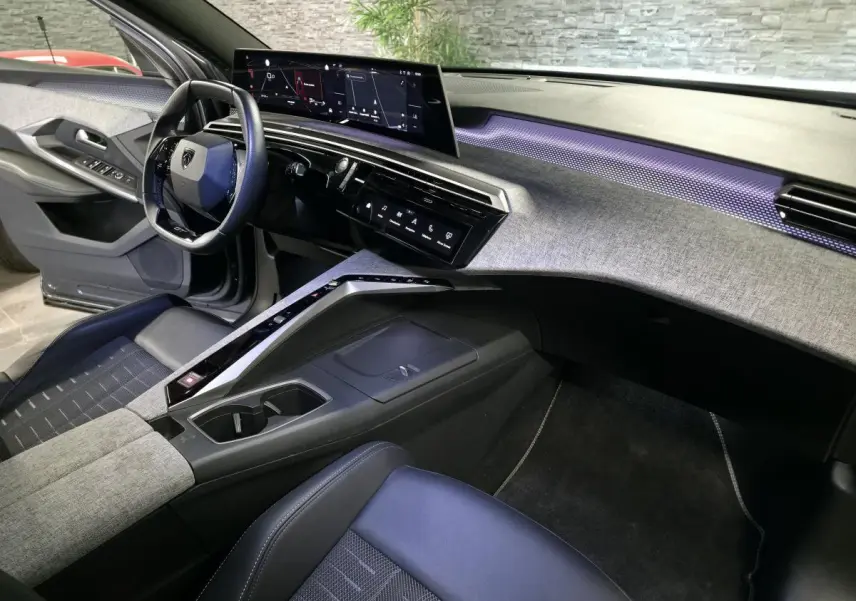 Vue intérieure côté conducteur du Peugeot 5008 gris 2025, avec planche de bord tissu Rimini et éclairage d'ambiance violet.