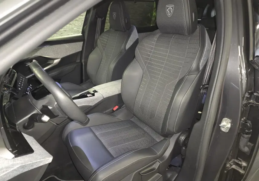 Vue intérieure côté conducteur du Peugeot 5008 gris 2025, sièges tissu et cuir avec logo Peugeot brodé sur les appuie-têtes.