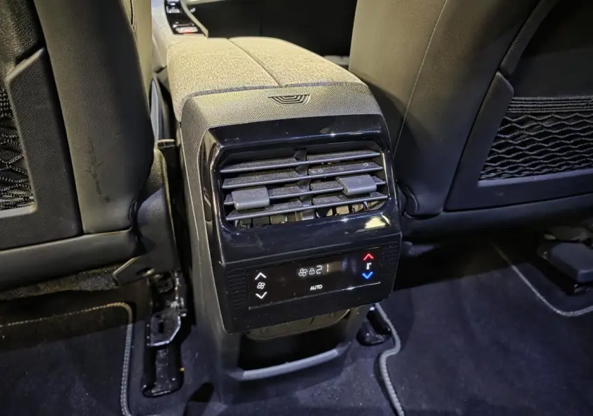 Vue rapprochée de la console centrale arrière du Peugeot 5008 gris, avec commandes de climatisation et aérateurs noirs laqués.