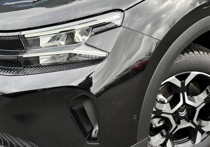 Gros plan sur l'avant droit noir Perla du Citroën C5 Aircross Hybrid, mettant en valeur le phare LED et la jante alliage bicolore.