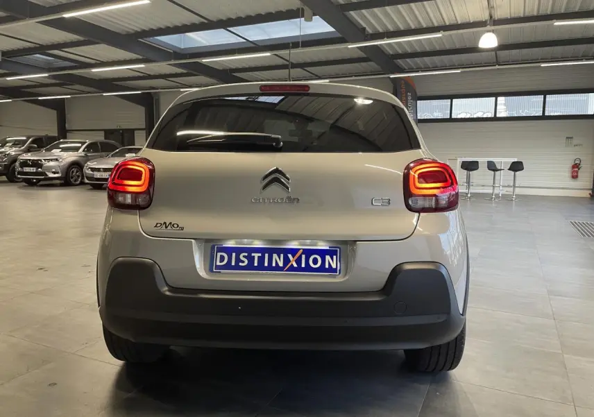 Vue arrière d'une Citroën C3 beige clair 2024 avec feux arrière à effet 3D et pare-chocs noir mat en intérieur showroom.