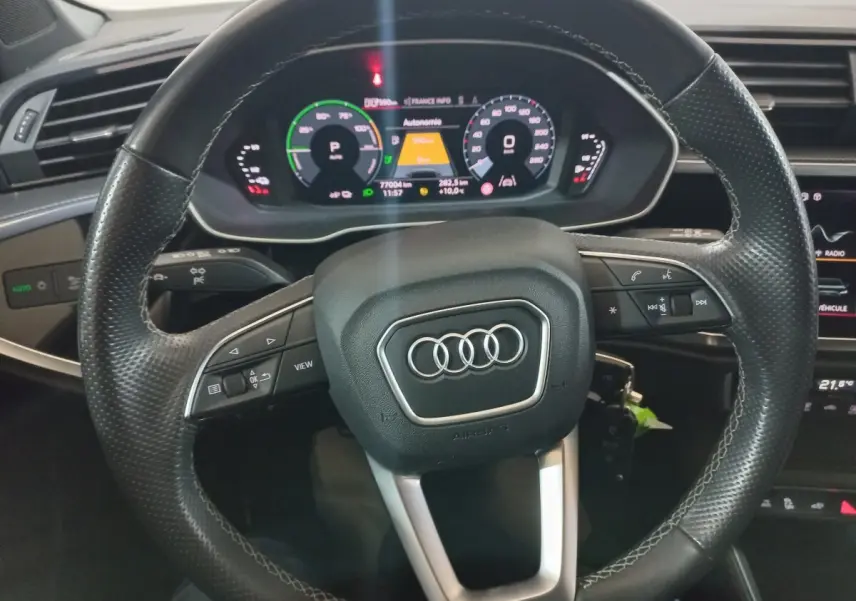 Vue rapprochée du volant cuir multifonctions et du tableau de bord numérique de l'Audi Q3 blanc hybride rechargeable.