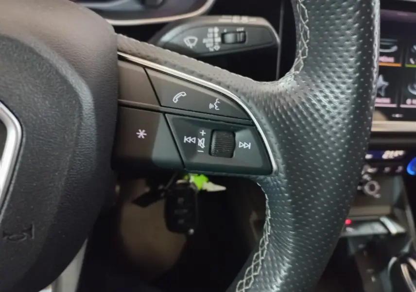 Gros plan sur la partie gauche du volant en cuir perforé de l'Audi Q3 blanc, avec commandes audio et téléphone intégrées.