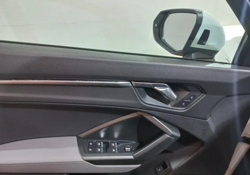 Vue intérieure côté gauche de la porte d’un Audi Q3 blanc, avec commandes de vitres et rétroviseur électrique.
