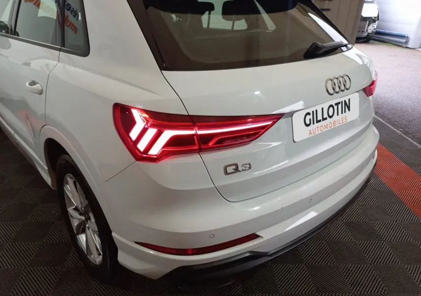 Vue 3/4 arrière droite d’un Audi Q3 blanc avec feux arrière LED allumés dans un showroom.