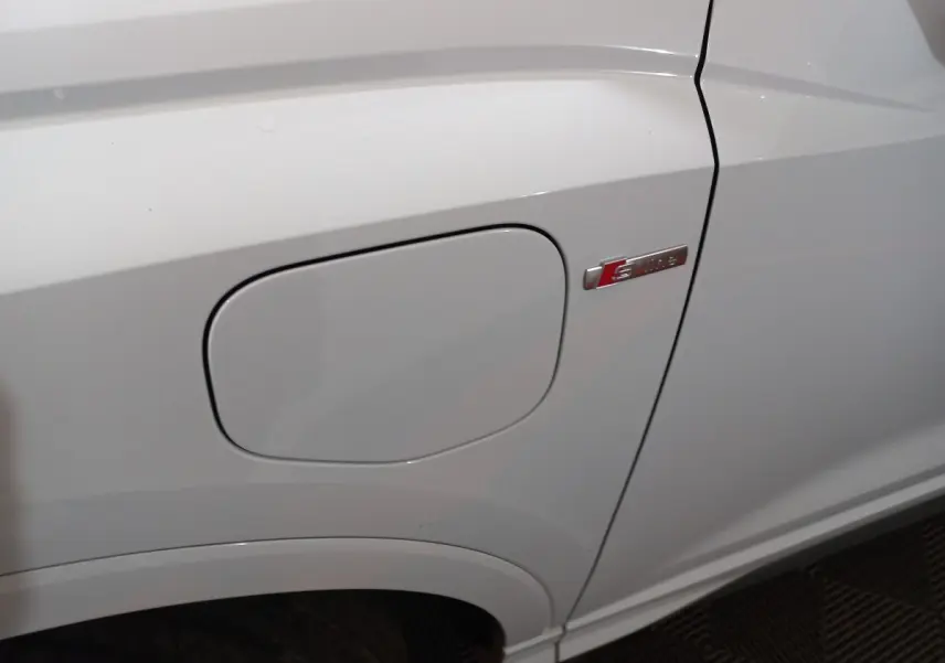 Gros plan sur la trappe de recharge côté gauche d’un Audi Q3 blanc avec badge S line visible.