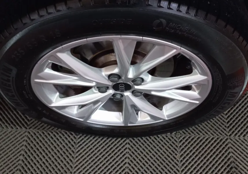 Gros plan sur la jante argentée en alliage de l'Audi Q3 blanc, avec pneu Michelin visible sur sol texturé.
