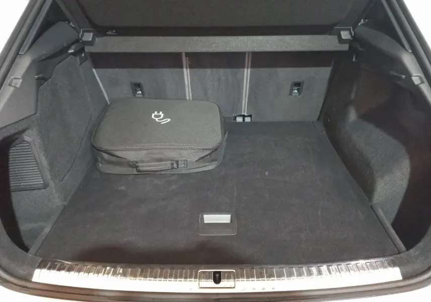 Coffre ouvert vu de face d’un Audi Q3 blanc hybride rechargeable, avec sac de charge noir posé à gauche.